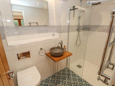 A bathroom with a toilet a stone sink on a wooden table and a glass-enclosed shower at Rudbaxton Water in Rudbaxton near Haverfordwest