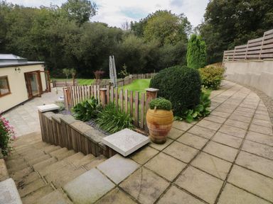 A paved outdoor area with steps leading down to a fenced grassy garden with shrubs and a large clay pot at Rudbaxton Water Rudbaxton near Haverfordwest
