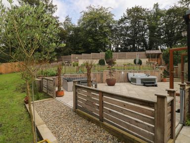 A backyard garden with a tiled patio area including seating and a hot tub surrounded by wooden fences and trees at Rudbaxton Water Rudbaxton near Haverfordwest