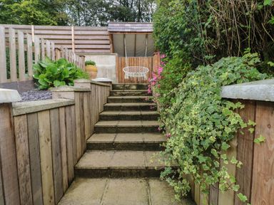 A garden pathway with stone steps flanked by wooden retaining walls and plants leading to a hanging chair at Rudbaxton Water Rudbaxton near Haverfordwest