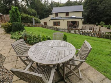 A wooden outdoor table with four chairs on a patio next to a garden and a house with fenced yard at Rudbaxton Water in Rudbaxton near Haverfordwest
