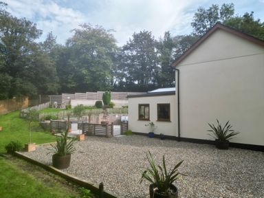 A garden with gravel area and potted plants next to a white house surrounded by trees at Rudbaxton Water in Rudbaxton near Haverfordwest