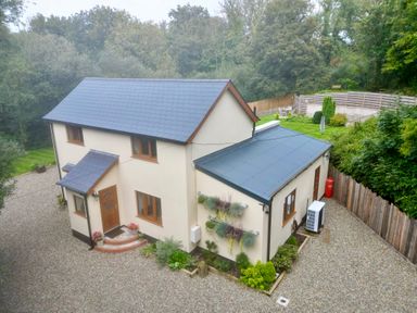 A two-story house with a slate roof and wooden windows surrounded by gravel and greenery at Rudbaxton Water in Rudbaxton near Haverfordwest