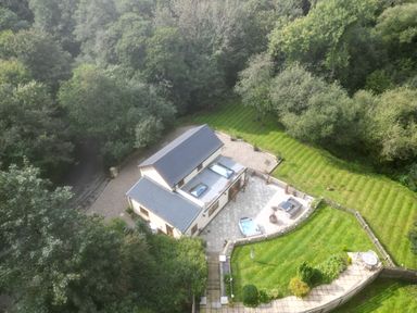 An aerial view of a house with a patio seating area and hot tub surrounded by lawn and trees at Rudbaxton Water Rudbaxton near Haverfordwest