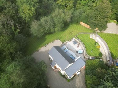 An aerial view of a house with a gray roof surrounded by trees and a lawn with a patio and outdoor seating at Rudbaxton Water in Rudbaxton near Haverfordwest