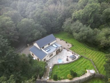An aerial view of a house with a patio hot tub and outdoor seating surrounded by a lawn and trees at Rudbaxton Water Rudbaxton near Haverfordwest