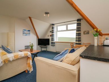 A living room with sofas cushions a coffee table a television and a dining table with chairs at 5 Seymour Villas in Woolacombe