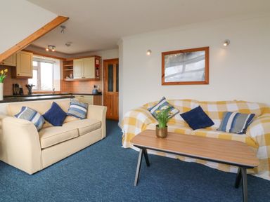 A living room with two sofas and a coffee table with flowers and an open kitchen in the background at 5 Seymour Villas in Woolacombe