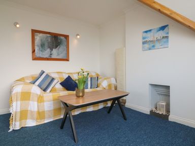 A living room with a yellow and white checked sofa a wooden coffee table with flowers on it and paintings on the walls at 5 Seymour Villas in Woolacombe