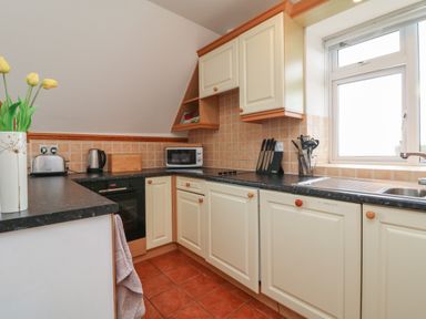 A kitchen with cream cabinets black countertop a window and a vase with yellow flowers at 5 Seymour Villas in Woolacombe