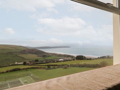 A coastal landscape with green fields and a beach viewed through a window at 5 Seymour Villas in Woolacombe