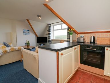 A small living room with sofas and a television next to a kitchen with oven toaster and kettle at 5 Seymour Villas Woolacombe
