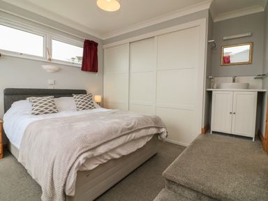 A bedroom with a bed, pillows, bedside table, a lamp, closet with sliding doors, sink, and mirror at 5 Seymour Villas in Woolacombe