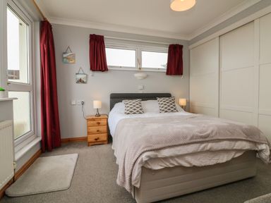 A bedroom with a double bed two bedside tables with lamps red curtains and a wardrobe with sliding doors at 5 Seymour Villas in Woolacombe