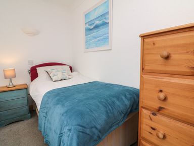 A bedroom with a single bed covered by a blue blanket next to a blue bedside table with a lamp and a wooden chest of drawers at 5 Seymour Villas in Woolacombe