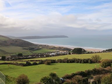 A coastal landscape with green fields, a small village, hills, and the ocean at 5 Seymour Villas in Woolacombe