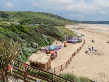 A sandy beach with amusement rides and green hills in the background at 5 Seymour Villas Woolacombe