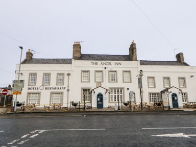 The exterior of The Angel Inn hotel and restaurant with benches on the sidewalk and road signs nearby