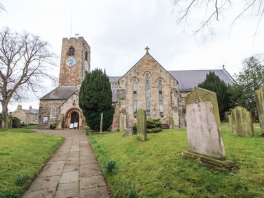A stone church with a clock tower and gravestones in a grassy churchyard at Willows Corbridge