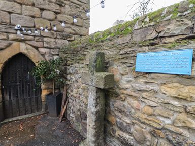 An old stone cross mounted on a stone wall next to a black wooden door with string lights hanging above at The Willows in Corbridge