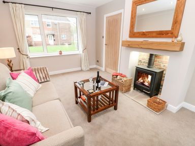 A living room with a beige sofa with cushions a wooden coffee table a wood burning stove and a window at Willows in Corbridge