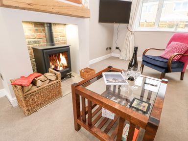A living room with a wood-burning stove basket of logs glass coffee table bottle of wine and two glasses at Willows in Corbridge