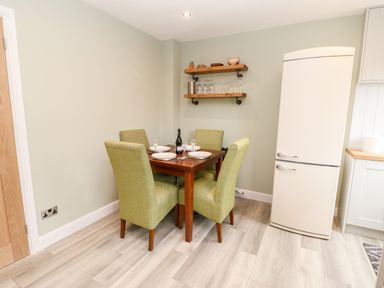 A dining area with a wooden table set for four with green chairs and a cream refrigerator at Willows in Corbridge