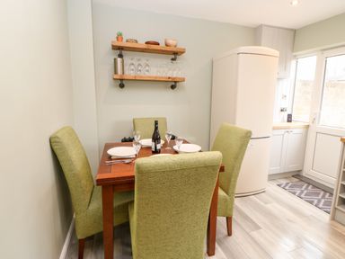 A dining area with a wooden table set with plates glasses and a bottle surrounded by green upholstered chairs in a kitchen at Willows in Corbridge