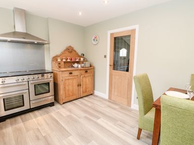 A kitchen with a stainless steel oven a wooden dresser a wooden door and green dining chairs at Willows in Corbridge