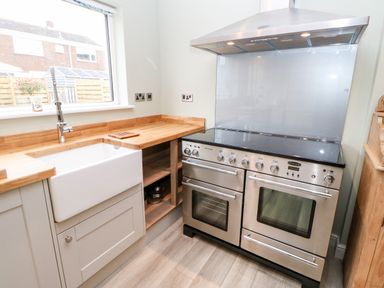 A kitchen with a large stainless steel stove and oven a white farmhouse sink wooden countertops and a window overlooking a fenced garden at Willows in Corbridge