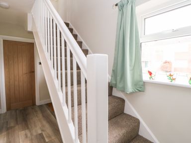 A carpeted staircase with white banisters next to a window with green curtains and a wooden door on a wooden floor at Willows in Corbridge