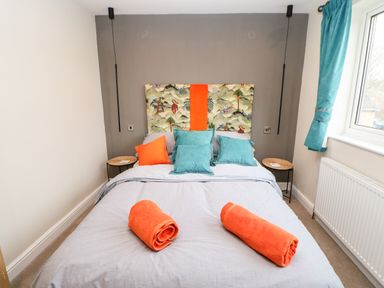 A bedroom with a bed with patterned headboard and turquoise and orange pillows at Willows in Corbridge