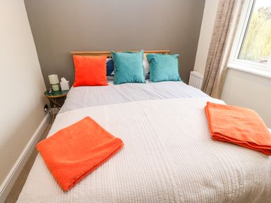 A bedroom with a bed with orange and teal pillows and orange towels on a white blanket at Willows in Corbridge