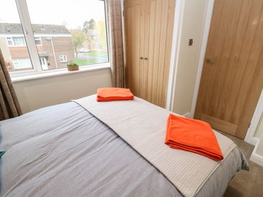 A bedroom with a bed folded orange towels on the bed near window and wooden doors at Willows Corbridge