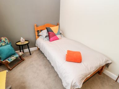 A single bed with pillows and a folded orange towel next to a small side table and a chair in a bedroom at Willows in Corbridge