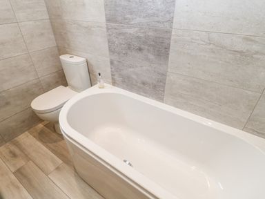 A bathroom with a bathtub and a toilet with tiled walls and wooden floor at Willows in Corbridge