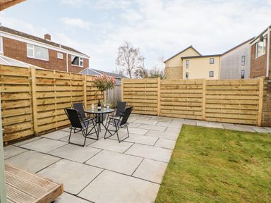 A backyard patio with a glass table and four chairs next to a wooden fence and a grass lawn at Willows in Corbridge