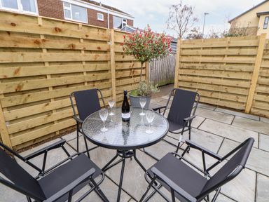 An outdoor patio area with a round glass table surrounded by four black chairs and a bottle with four glasses at Willows in Corbridge