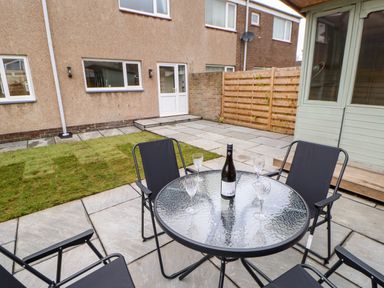 A patio with a round glass table and four black chairs beside a lawn and a wooden fence at Willows in Corbridge