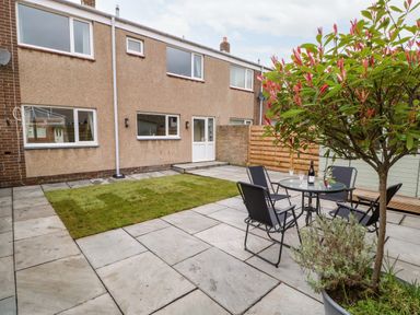 A backyard with a small grass area a patio table with four chairs a potted tree and a two story house at Willows in Corbridge