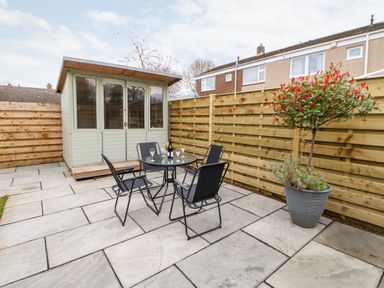 A patio with a glass table and four chairs a potted plant a wooden shed and a wooden fence at Willows in Corbridge