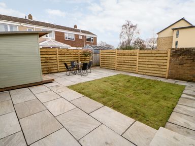 A backyard with a grassy area a patio with a table and four chairs and a shed at Willows in Corbridge