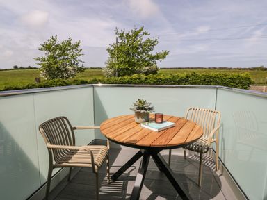 A balcony with a round wooden table two chairs a plant a book and a candle at The Hayloft in Llanfechell