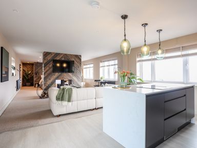 An open-plan living room and kitchen with a white sofa a wooden feature wall with a mounted tv a kitchen island with pendant lights and large windows at The Hayloft in Llanfechell