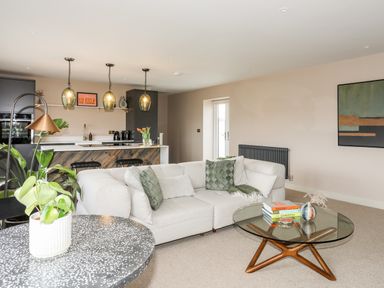An open living room and kitchen with a beige sofa and glass coffee table at The Hayloft in Llanfechell