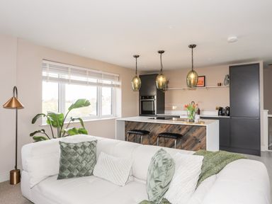 An open plan living room and kitchen with a white sofa with green pillows and a kitchen island with pendant lights at The Hayloft in Llanfechell