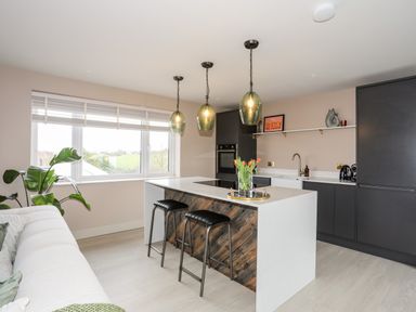 A modern kitchen with a central island and bar stools next to a window at The Hayloft in Llanfechell