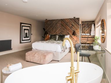 A bedroom with a bed a bathtub with gold faucet a desk and chair and wooden wall panels at The Hayloft in Llanfechell