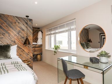 A bedroom with a bed with pillows and blanket a glass desk with a chair a round mirror and a window at The Hayloft in Llanfechell