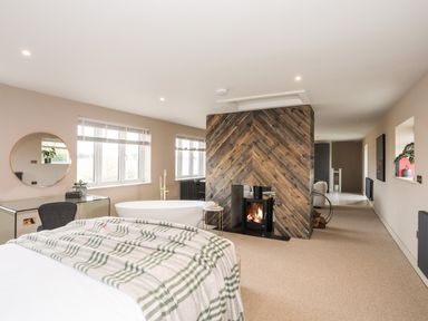 A bedroom with a bed a fireplace a bathtub and a desk near windows at The Hayloft in Llanfechell